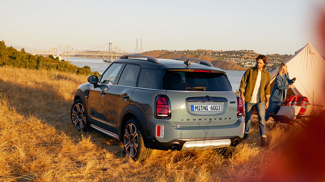 Ein blauer SUV steht auf einem Feld vor einem Fluss, im Hintergrund eine Brücke.