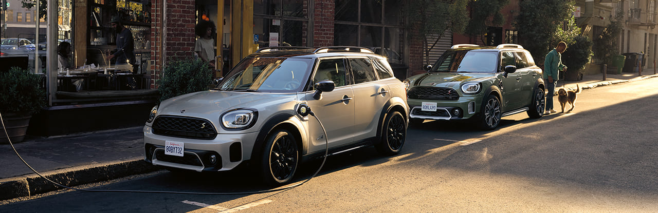 Zwei MINI Countryman parken auf der Straße, einer wird aufgeladen, Menschen in der Nähe.