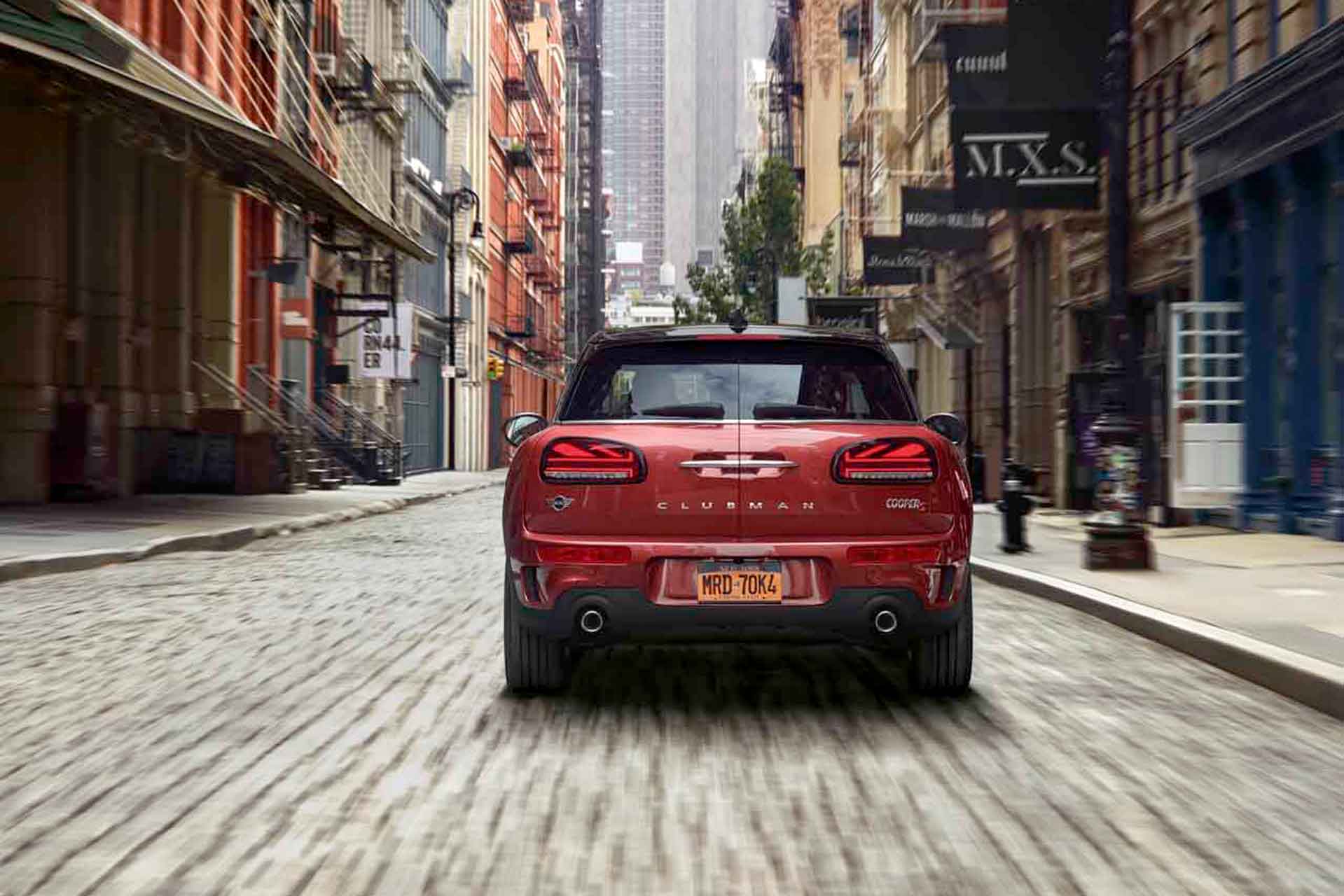 Roter MINI Clubman fährt auf leerer Kopfsteinpflasterstraße in städtischer Umgebung.