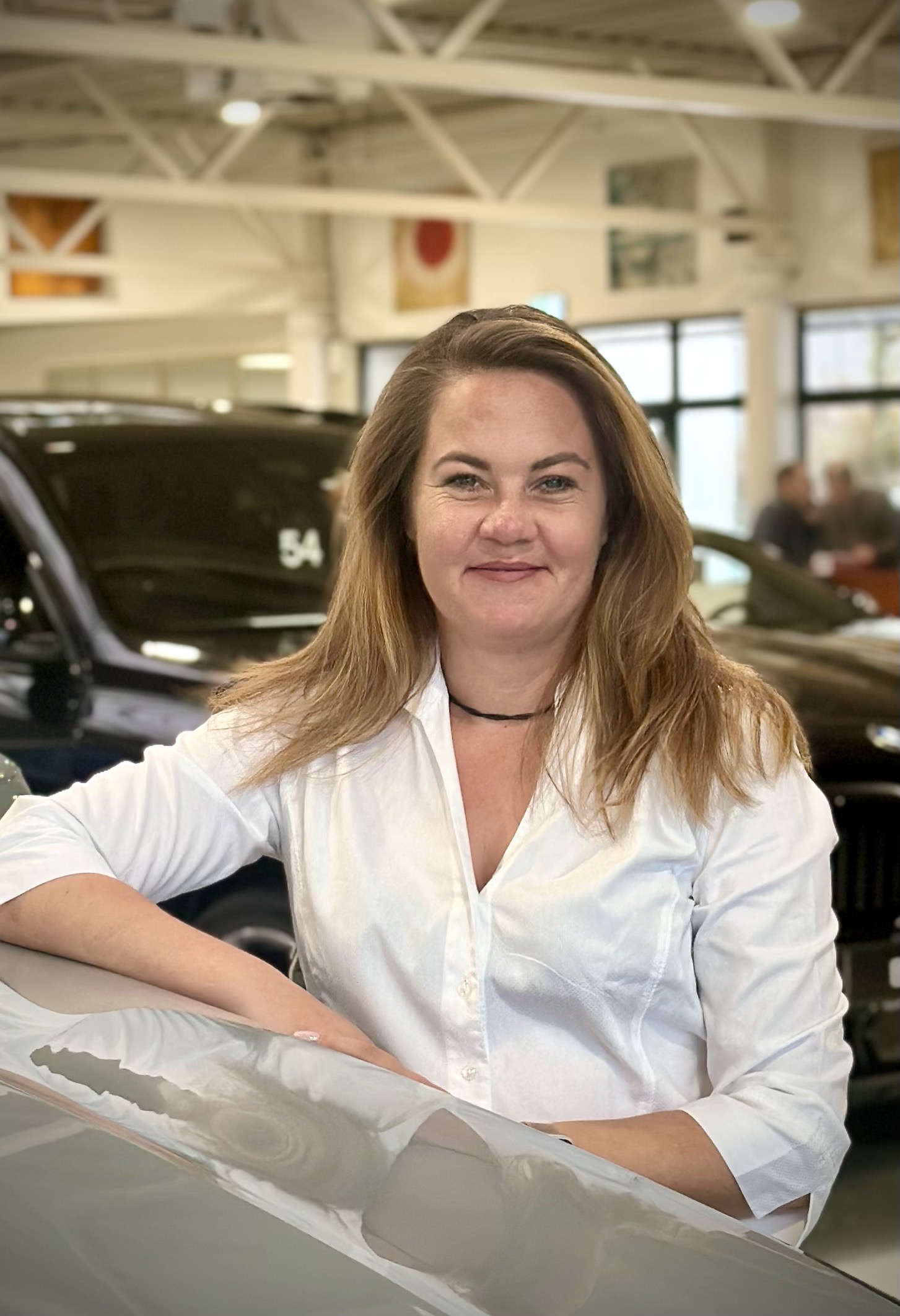 Frau in weißem Hemd steht in einem Autohaus, Autos im Hintergrund. MINI Mülheim.