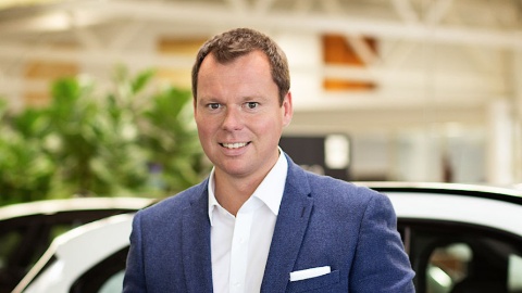 Mann in blauem Sakko vor einem Auto in einem Autohaus.