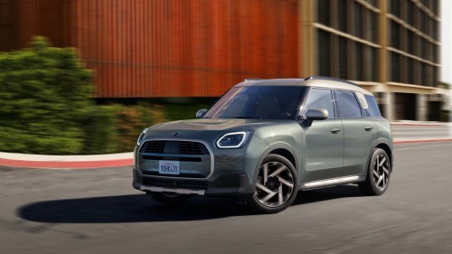 Grüner SUV auf Straße vor modernen Gebäuden und Bäumen bei Sonnenschein.