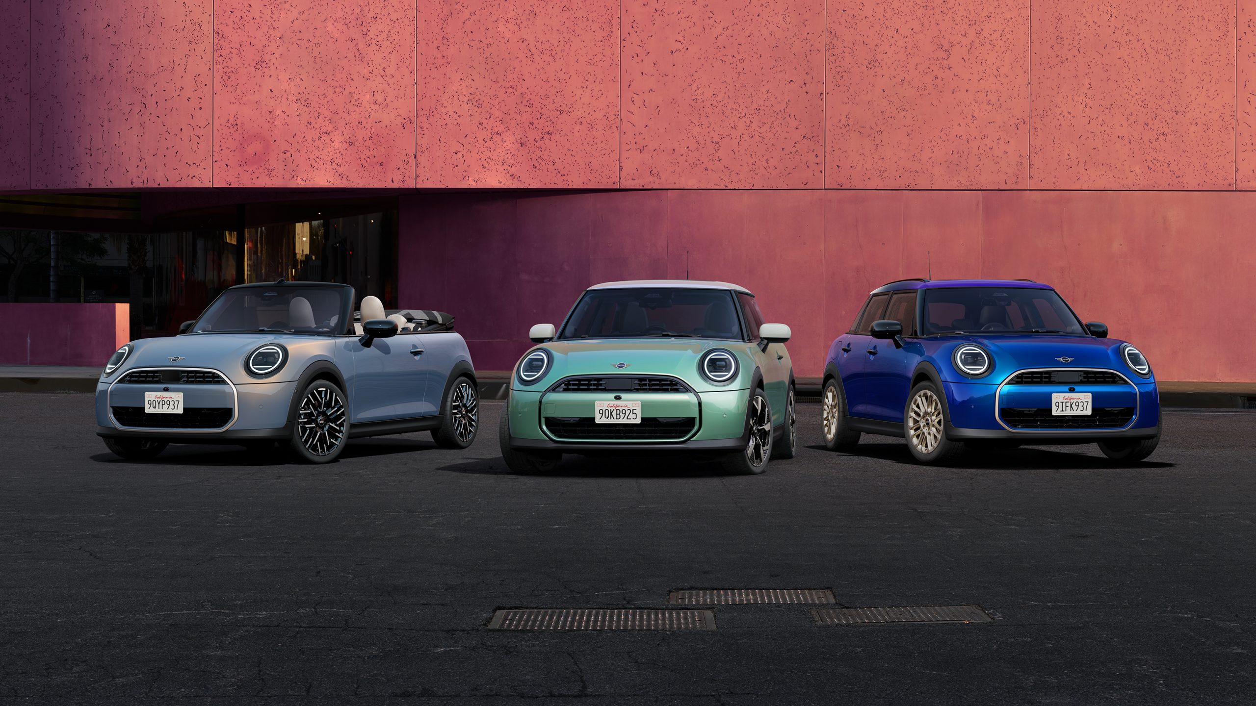 Drei bunte MINI Cooper vor rosa Wand: grau, türkis, blau.