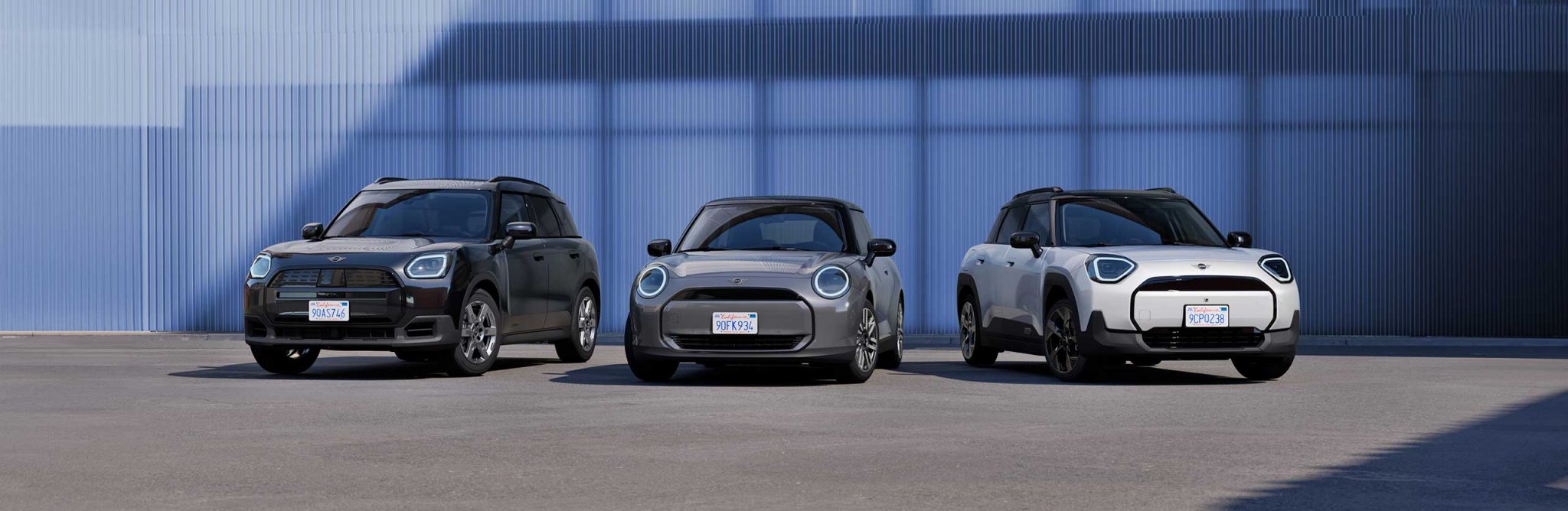 Drei MINI-Autos nebeneinander vor blauer Wand auf Asphaltfläche.